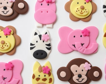 Op de afbeelding: Een verzameling platte fondant dierfiguren, bestaande uit een bruine aap, een roze nijlpaard, een gele leeuw, een zwart-witte zebra, een roze olifant en een gele giraf, elk versierd met een klein roze of lichtroze bloemetje.
