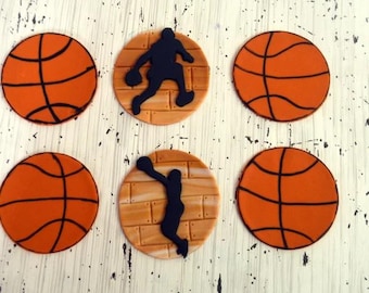 May include: Six circular edible decorations featuring four orange basketballs with black lines and two tan circular discs with a brick pattern, each topped with a black silhouette of a basketball player in a dynamic jumping or dunking pose.
