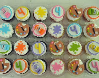 Op de afbeelding: Een set van vierentwintig cupcakes in een plastic tray, elk voorzien van witte glazuur en fondantdecoraties waaronder het cijfer 4, verfspatten, verftubes met het opschrift PAINT en kunstenaarspaletten met penselen in diverse kleuren.