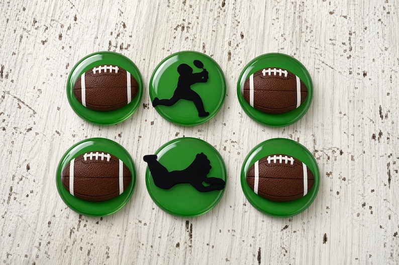 May include: A set of six circular green buttons featuring raised designs. Four buttons display a brown American football with white laces, while two buttons feature a black silhouette of a football player in different athletic poses.