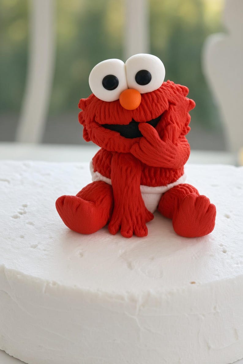 May include: A red, textured fondant figurine of a character with large white eyes, black pupils, and an orange nose. The figure is sitting down, wearing a white diaper, and has one hand raised to its mouth. The character has a fuzzy appearance.