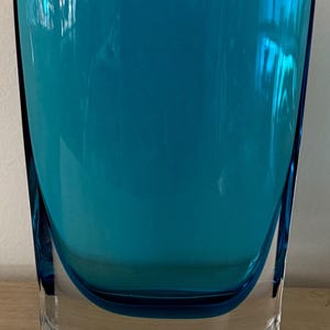 May include: A rectangular glass vase featuring a deep teal blue interior encased in clear glass. The vessel has a wide, flat top opening and a thick, solid base, showcasing a smooth, polished surface with clean, sharp edges and a transparent finish.