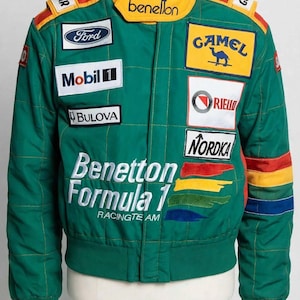 Può includere: Una giacca da corsa verde Benetton Formula 1 con colletto giallo, strisce rosse e gialle sulle spalle e strisce multicolori sulle maniche. La giacca presenta varie toppe di sponsor tra cui Ford, Mobil 1, Bulova, Camel, Riello e Nordica.