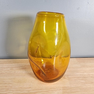 May include: A clear amber glass vase with a unique, organic shape. The vase has a wide mouth and a narrow base.