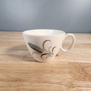 Peut inclure: Une tasse à thé en céramique blanche avec un motif floral brun et bleu. La tasse a une forme arrondie et une anse.