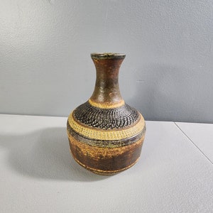 May include: A brown and black ceramic vase with a textured design. The vase has a wide base and a narrow neck.