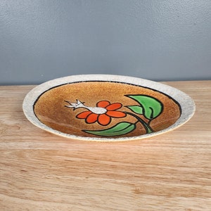 May include: A brown ceramic dish with a white rim and a hand-painted orange flower with green leaves.