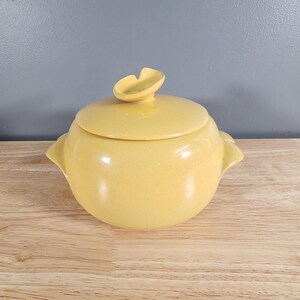 Peut inclure: Un plat couvert en céramique jaune avec un bouton en forme de feuille unique sur le couvercle. Le plat a deux petites poignées sur les côtés.