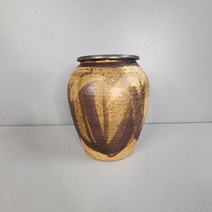 May include: A brown and yellow ceramic vase with a dark brown abstract design. The vase has a rounded body and a slightly flared lip.