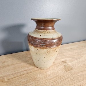 May include: A ceramic vase with a brown and white glaze. The vase has a wide mouth and a narrow base. It is decorated with a brown band around the middle.