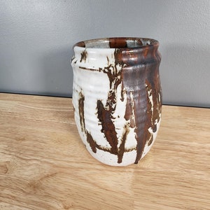 May include: A white ceramic vase with brown glaze dripping down the sides. The vase has a rounded shape and a slightly flared lip.