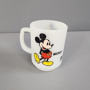 May include: White ceramic mug with a black and white image of Mickey Mouse wearing red shorts and yellow shoes. The mug says "Mickey" on the side.