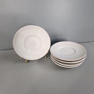 May include: Set of four white ceramic saucers. The saucers are stacked on top of each other. The saucers are plain and have a smooth, glossy finish.