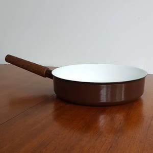 May include: A brown enamel frying pan with a white interior and a wooden handle.