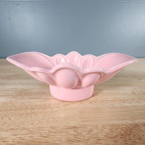 May include: A pink ceramic bowl with a scalloped edge and a raised centre. The bowl is shaped like a flower and has a delicate design.