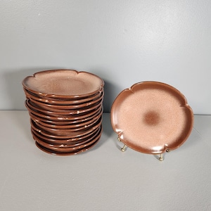May include: A stack of 12 brown and pink ceramic dessert plates with scalloped edges. One plate is displayed separately on a gold stand.