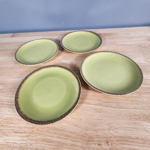 May include: Four green ceramic plates with a brown rim. The plates are on a wooden surface.