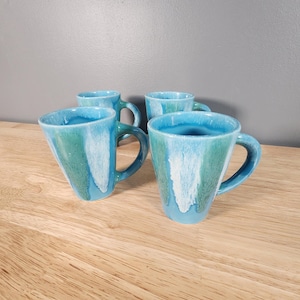 May include: Set of four blue and green ceramic mugs with a white glaze. The mugs have a unique, hand-painted design.