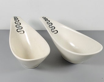May include: Two white ceramic serving dishes with black wavy lines. The dishes are shaped like a teardrop and are slightly angled.