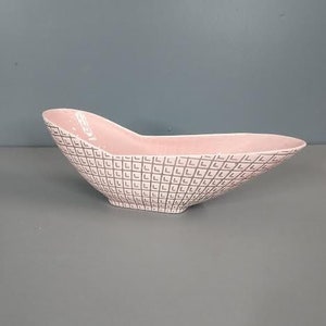May include: A pink, boat-shaped ceramic bowl with a geometric pattern. The bowl has a wide, open top and tapers to a point at the base. The pattern is a repeating grid of small squares and lines.
