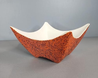 May include: A white and orange ceramic bowl with a textured surface. The bowl has a unique, geometric shape.