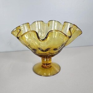 May include: A clear amber glass candy dish with a ruffled rim and a pedestal base.