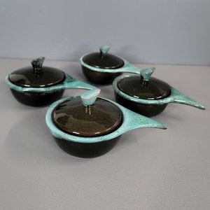 May include: Set of four small ceramic bowls with lids. The bowls are black with a turquoise rim and a turquoise knob on the lid. The bowls have a spout on one side.