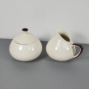 May include: A white ceramic sugar bowl and creamer set with brown trim and a speckled finish.