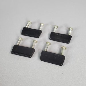 Peut inclure: Quatre boutons de cabinet noirs avec des vis argentées. Les boutons sont rectangulaires et ont un bord légèrement arrondi.
