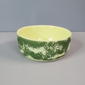 May include: A small, green and yellow ceramic bowl with a speckled pattern. The bowl is round and has a smooth, glossy finish.