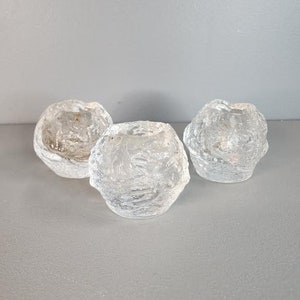 May include: Three clear glass candle holders with a textured, frosted finish. The candle holders are round and have a slightly uneven surface.
