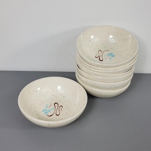 May include: A set of eight white ceramic bowls with a speckled brown and white glaze. Each bowl features a blue and brown floral design.