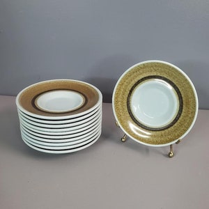 May include: A stack of 12 brown and white ceramic saucers with a gold metal stand holding a single saucer.