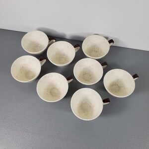 Puede incluir: Ocho tazas de caf&eacute; color crema moteadas con asas marrones oscuras dispuestas sobre una superficie gris. Las tazas tienen forma redondeada y un patr&oacute;n moteado, lo que sugiere un estilo vintage. Las asas son de color marr&oacute;n oscuro.