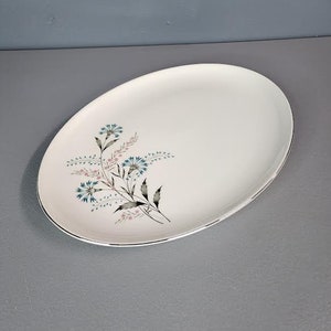 May include: A white oval serving platter with a floral design featuring blue and pink flowers and green leaves.