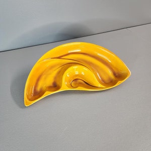 May include: A yellow and brown ceramic serving dish with three sections. The dish is shaped like a crescent moon and has a wavy design.