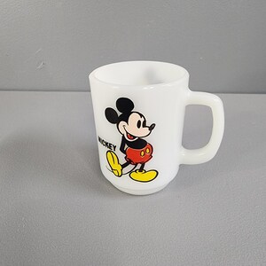 May include: White ceramic mug with a cartoon image of Mickey Mouse in red shorts and yellow shoes. The text "MICKEY" is printed on the mug.