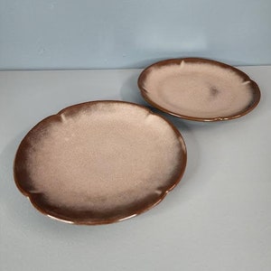 May include: Two brown ceramic plates with a light brown glaze. The plates have a scalloped edge and are slightly raised in the center.