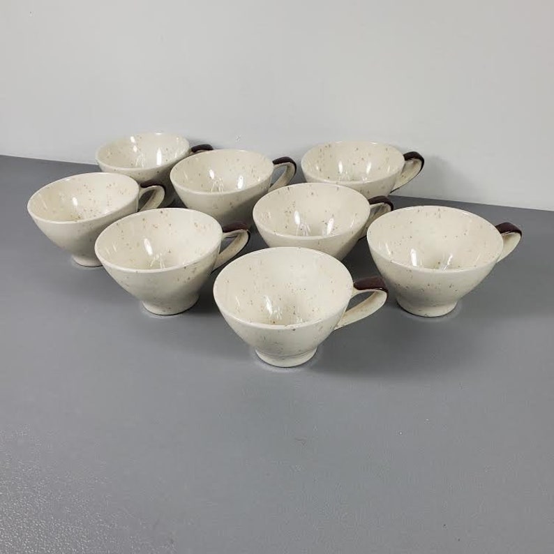 Puede incluir: Un juego de ocho tazas de t&eacute; color crema con detalles moteados. Cada taza tiene un asa marr&oacute;n oscuro. Las tazas est&aacute;n dispuestas en un patr&oacute;n circular ligeramente desplazado. Perfectas para servir t&eacute; o caf&eacute;.