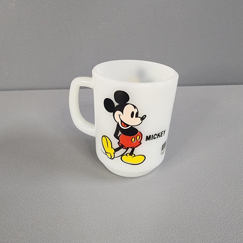 May include: White ceramic mug with a black and white image of Mickey Mouse wearing red shorts and yellow shoes. The mug says "Mickey" on the side.