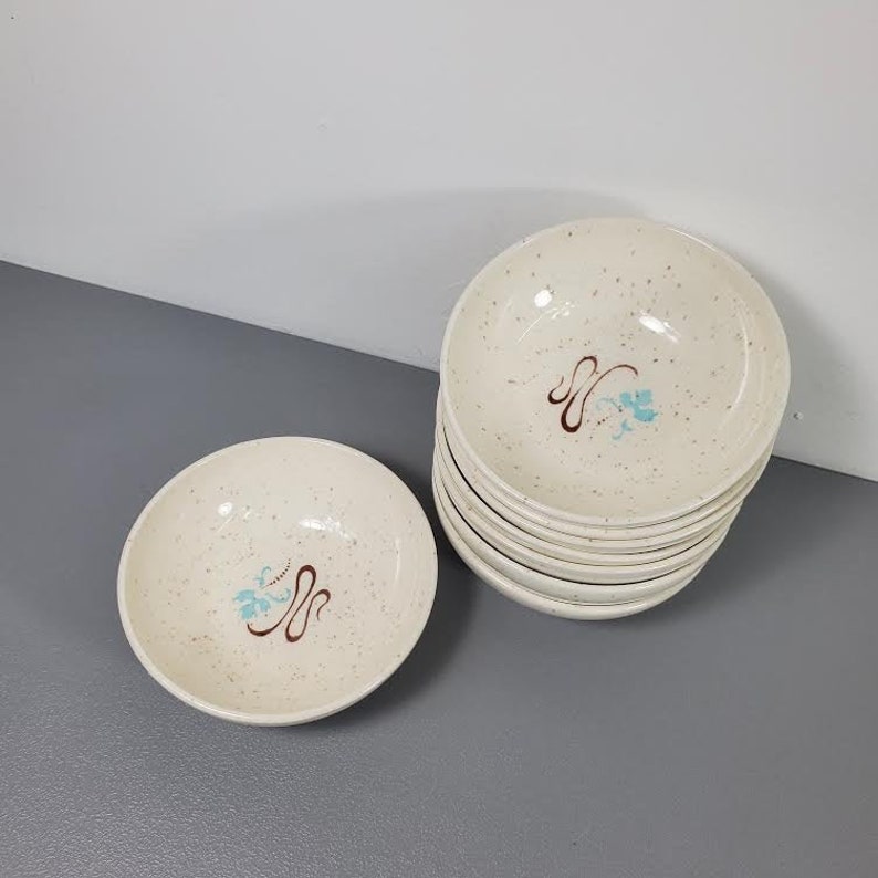 May include: A set of ten white ceramic bowls with a speckled finish. Each bowl features a brown and blue floral design.