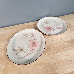 May include: Two white ceramic plates with a brown rim and a floral design. The design features pink flowers with brown stems and leaves.