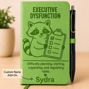 Peut inclure: Un carnet vert citron illustr&eacute; d'un raton laveur tenant un presse-papier, avec le texte "EXECUTIVE DYSFUNCTION", "Difficulty planning, starting, organizing, and regulating tasks" et le nom "Sydra". Un stylo noir est fix&eacute; sur le c&ocirc;t&eacute;.