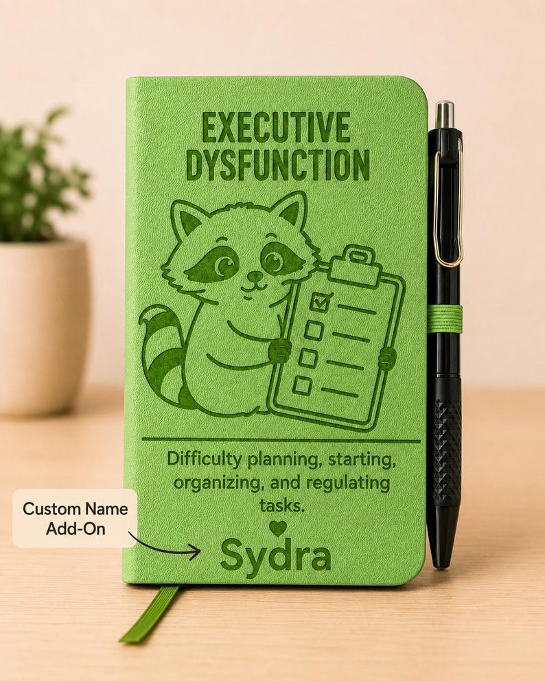 Peut inclure: Un carnet vert citron illustr&eacute; d'un raton laveur tenant un presse-papier, avec le texte "EXECUTIVE DYSFUNCTION", "Difficulty planning, starting, organizing, and regulating tasks" et le nom "Sydra". Un stylo noir est fix&eacute; sur le c&ocirc;t&eacute;.