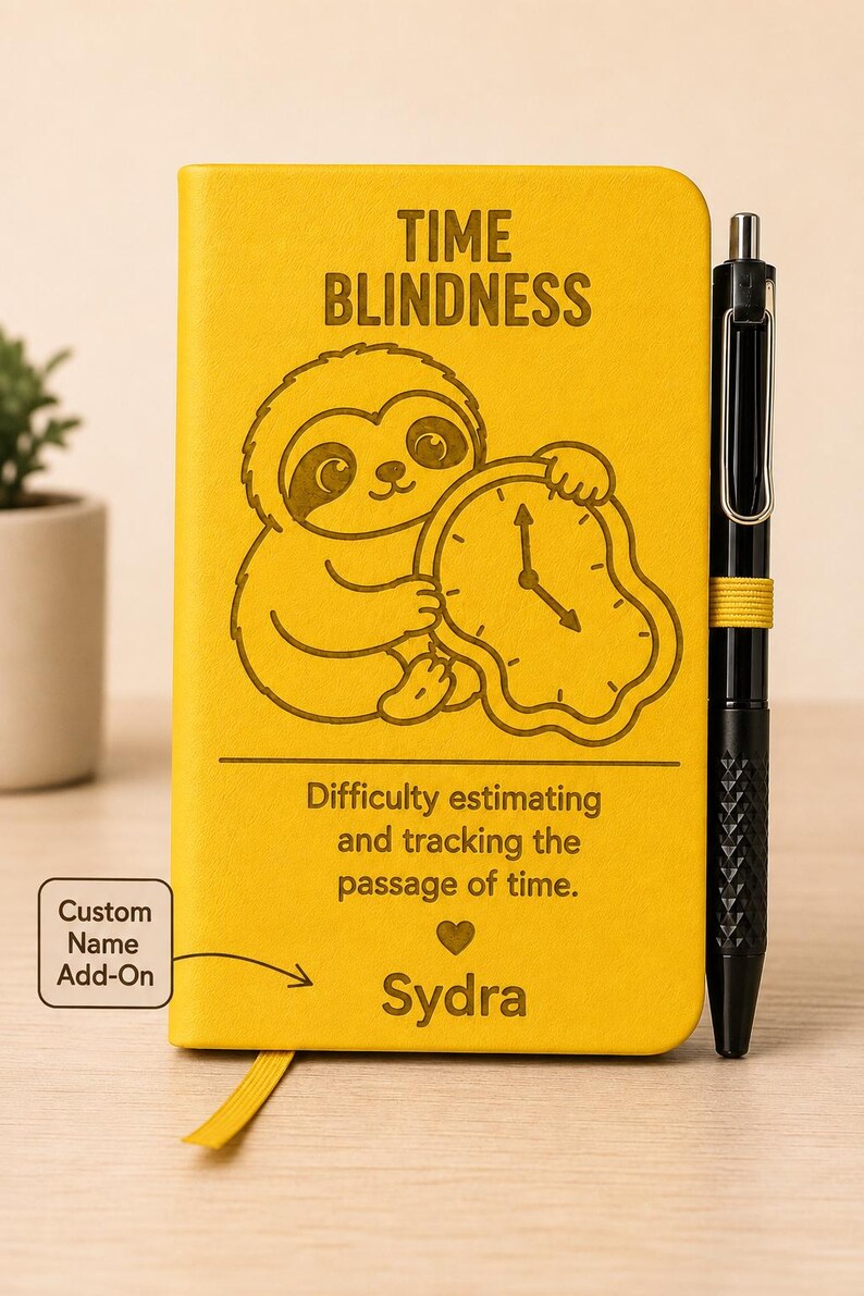 May include: A bright yellow notebook featuring a sloth holding a melting clock, with the text TIME BLINDNESS, Difficulty estimating and tracking the passage of time, and the name Sydra. A black pen is attached to the side of the notebook.