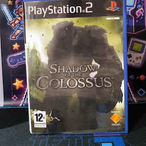 Może przedstawiać: Etui na grę wideo PlayStation 2 Shadow of the Colossus. Okładka przedstawia dużą, ciemną, kamienną postać w krajobrazie. Tytuł Shadow of the Colossus jest nadrukowany na środku, a w rogu znajduje się oznaczenie klasyfikacji wiekowej PEGI 12+.