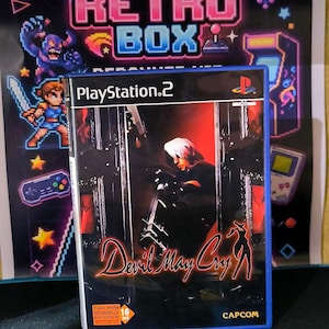 May include: A PlayStation 2 video game case for Devil May Cry featuring a character with white hair in a dark setting, the Capcom logo, and a 16 age rating label. The case is positioned in front of a poster labelled The Retro Box and a Tetris mat.