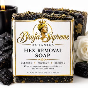 May include: A rectangular bar of black soap with embedded gold-toned particles. The label features a gold crown and profile illustration, with the text: Bruja Supreme Botanica, Hex Removal Soap, Cleanse, Protect, Remove, and Handcrafted with Spirit.