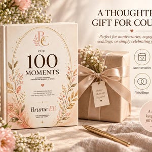 May include: A hardcover book titled Our 100 Moments by Brume Eli with a cream cover featuring gold floral illustrations and text. The book is displayed next to a gift-wrapped box with a ribbon, a gold pen, and a small tag reading Better Moments Together.