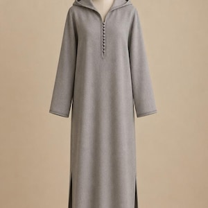 May include: A long-sleeved, floor-length hooded dress in a solid light gray color. The garment features a V-neckline adorned with a vertical row of small, matching fabric-covered buttons and includes high side slits along the lower hem.